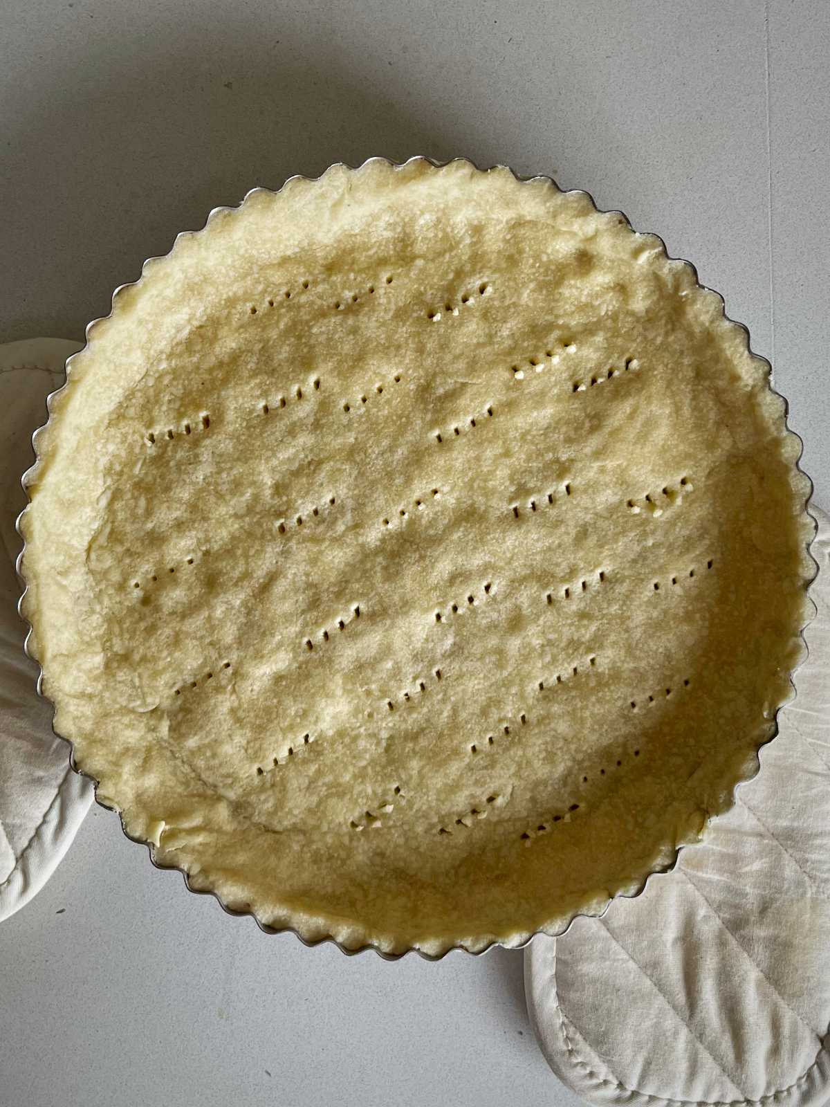Round tart shell baked in a pan with fork holes poked in the base.