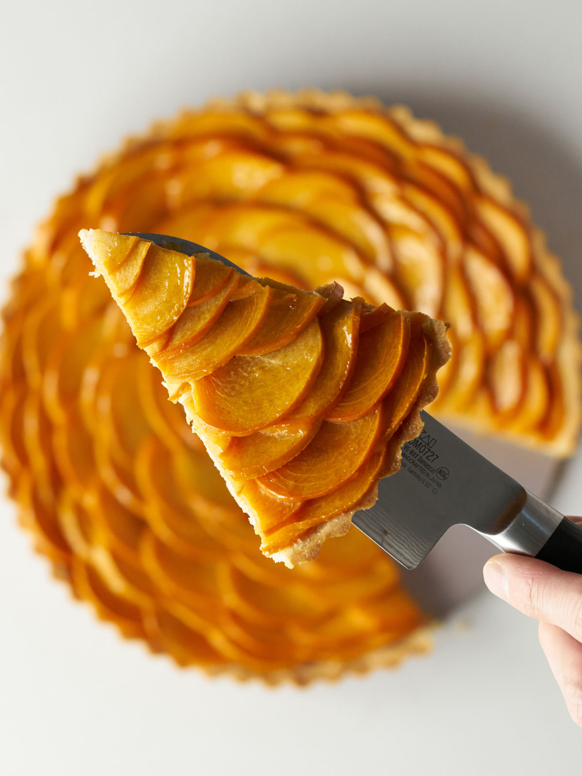 Slice of layered persimmon tart held up on a knife over the rest of the tart.