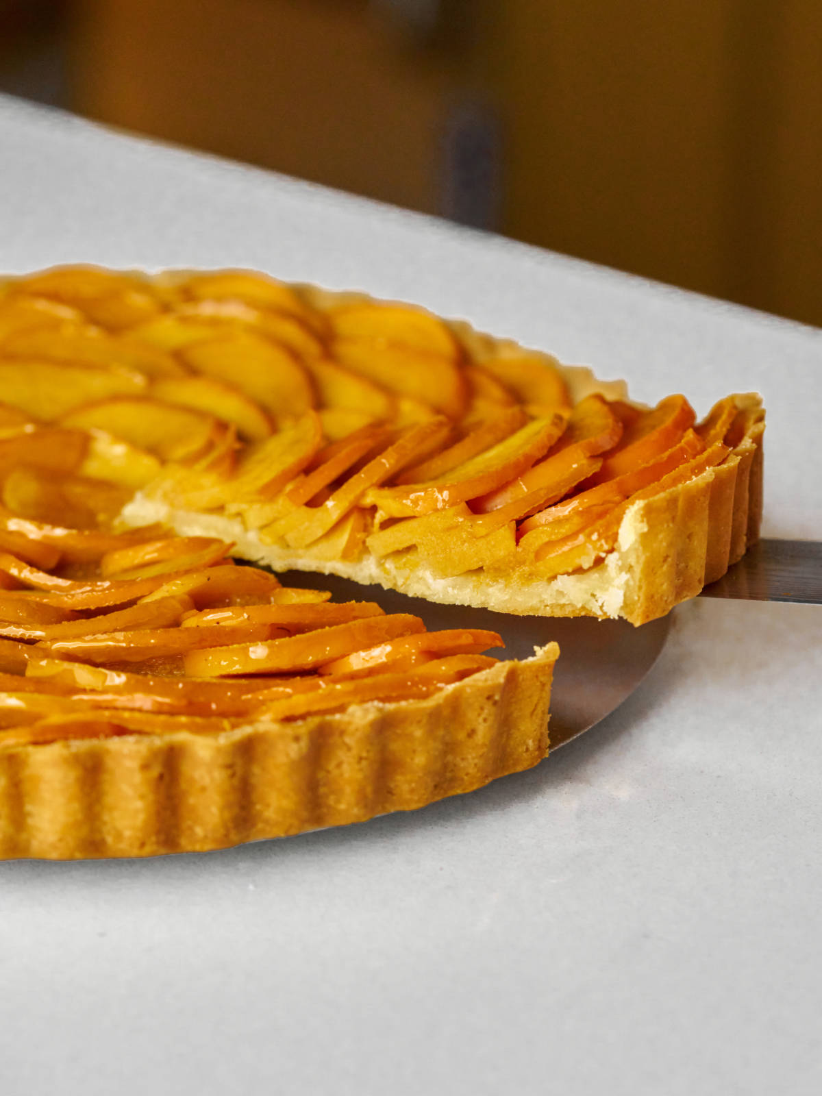 Slice of fruit tart being cut out of a tart on a metal disc.