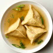 Top view of triangular dumplings in chicken broth with fresh herbs.