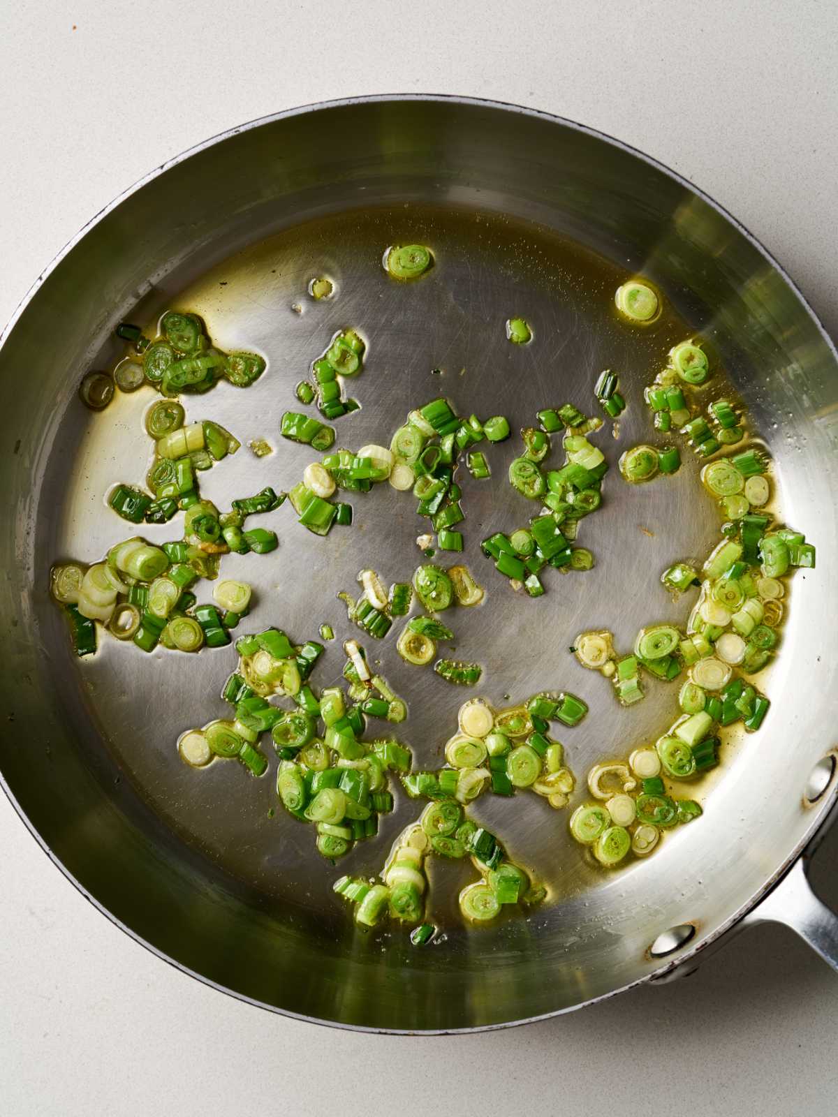 A silver pan containing oil and chopped scallions