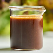 Salad dressing in a small beaker in front of lettuce.