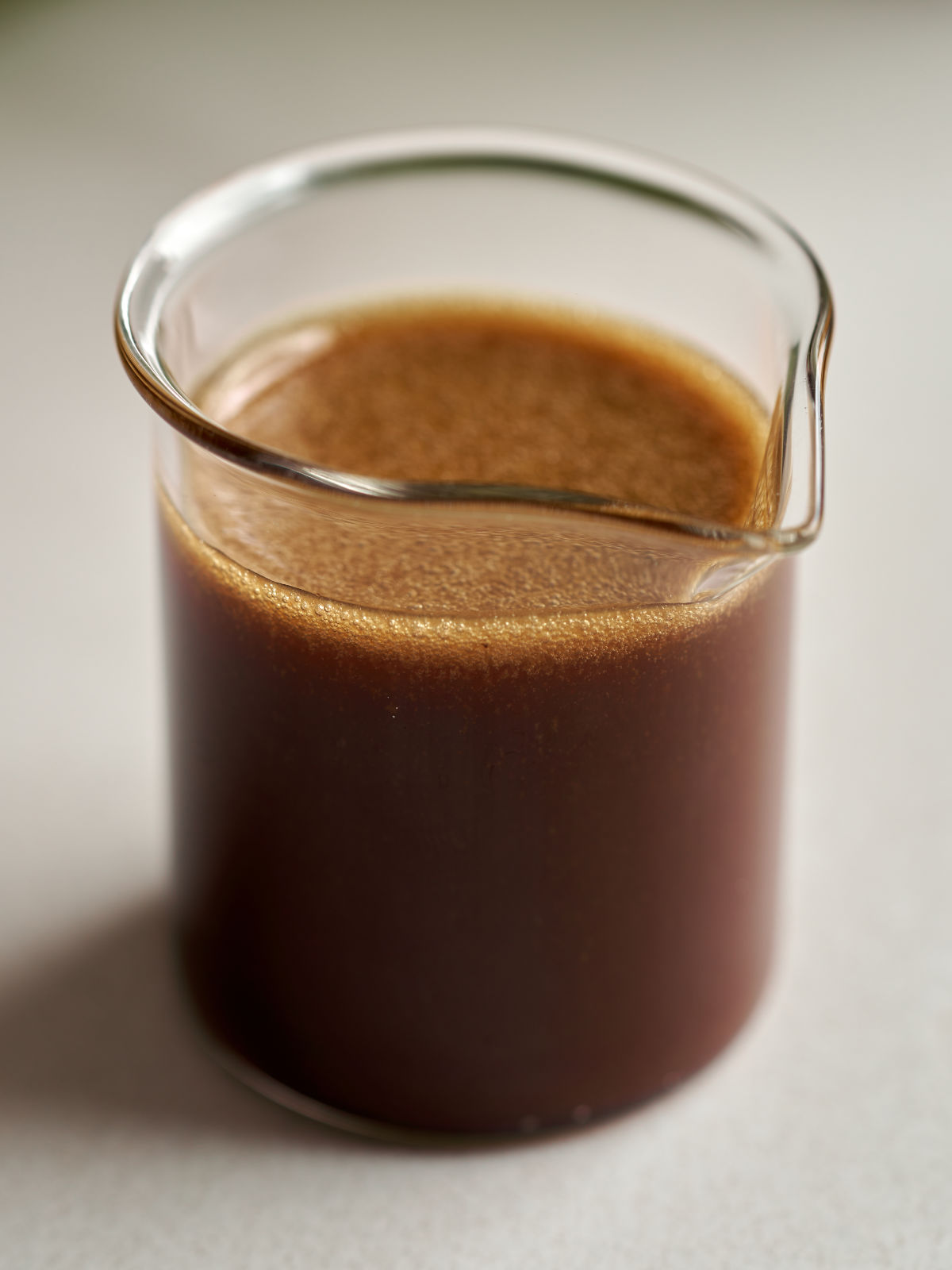 Brown salad dressing in a small beaker on a countertop.