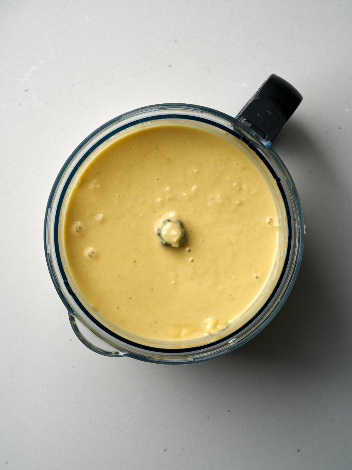 Yellow batter in a food processor bowl with a black handle.