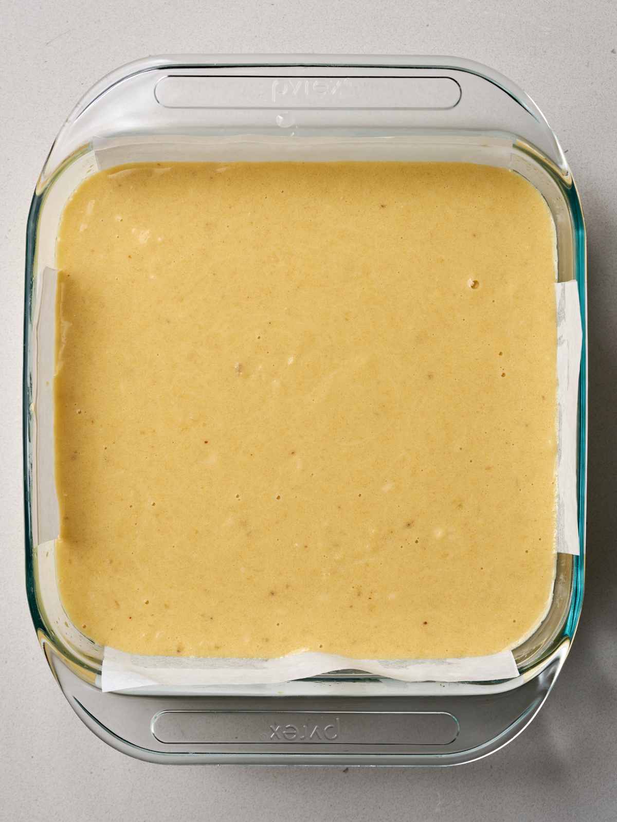 Raw yellow batter in a glass baking dish lined with parchment paper.