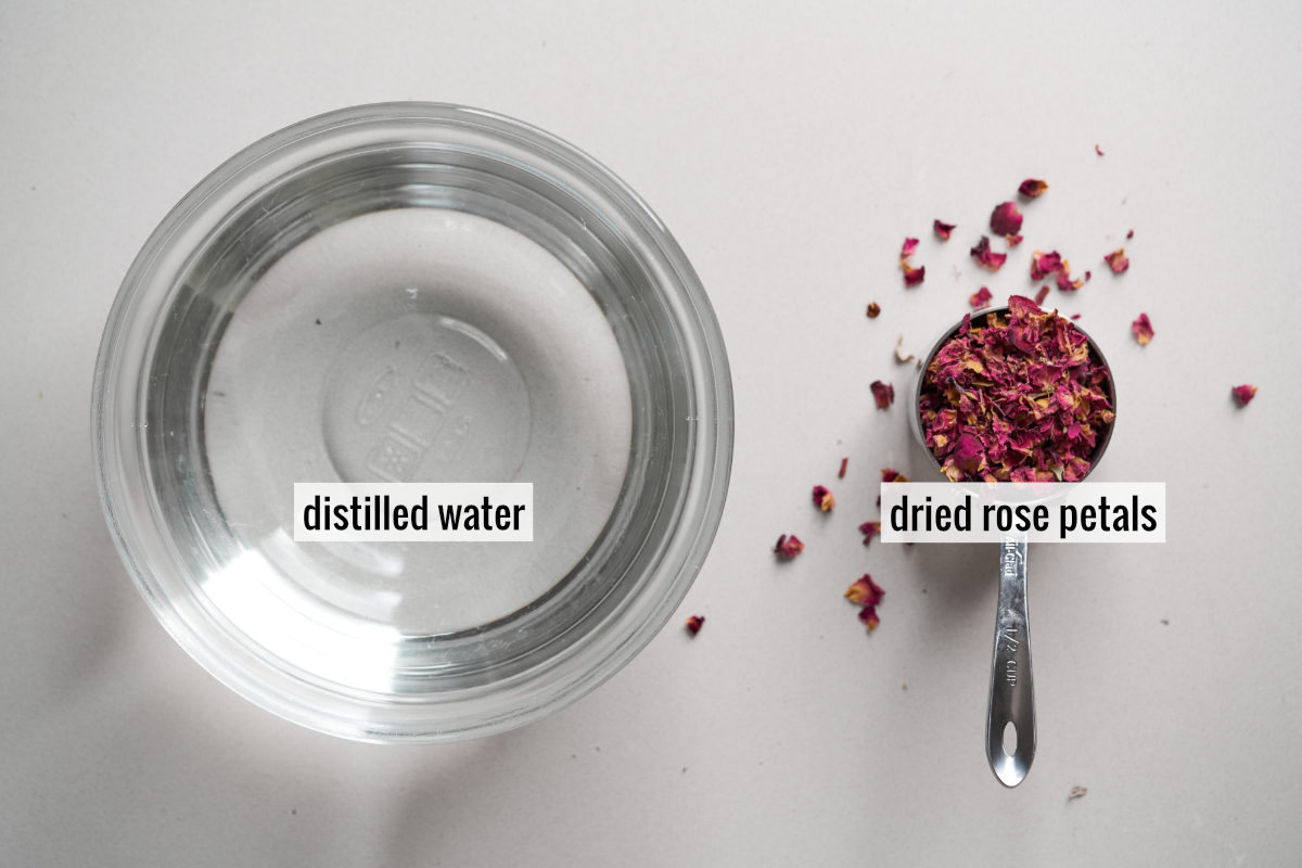 Tiny hot pink dried rose petals in a metal measuring cup next to a glass bowl filled with water.