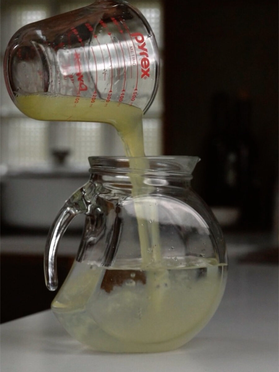 Lemon juice being poured into a large glass pitcher of water.