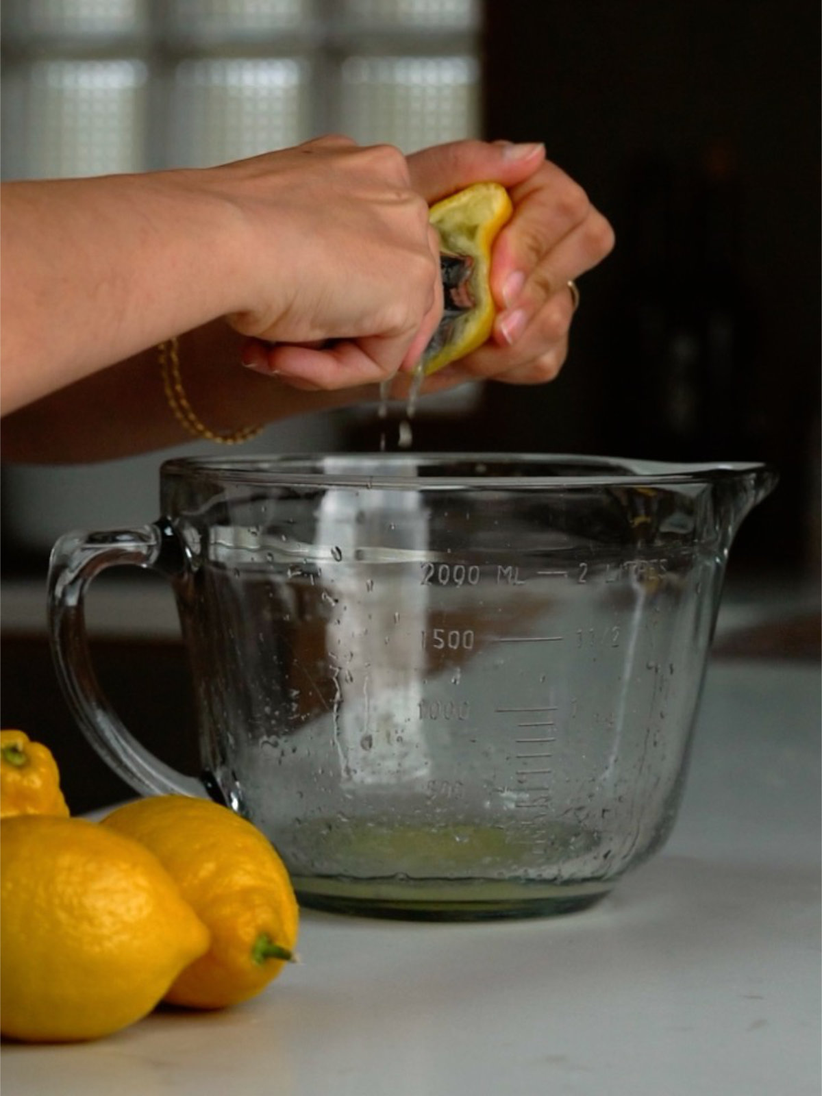 Two hands squeezing a lemon half over a large liquid measuring cup.