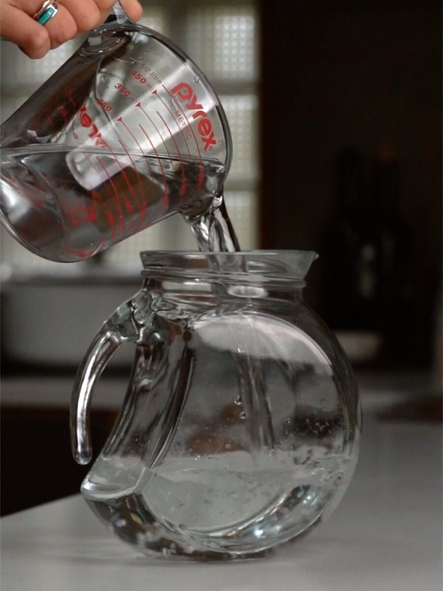 Water being poured from a glass pyrex glass into a large pitcher.