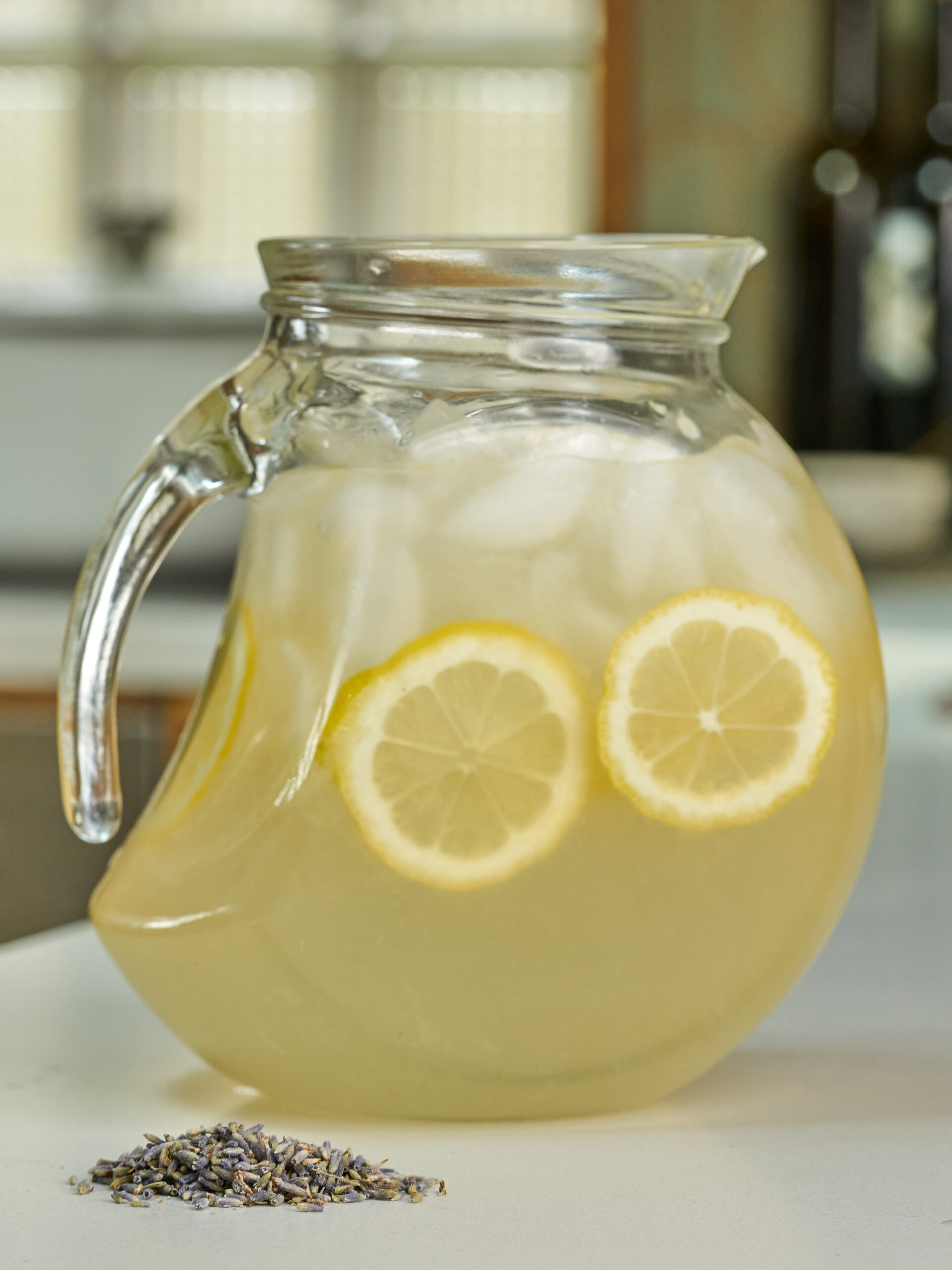 Pitcher with lemonade, lemon slices, and ice next to lavender buds.