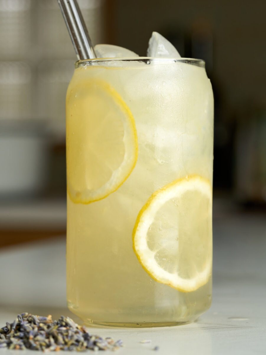 Lemonade in a beer can glass with lemon slices next to lavender buds.