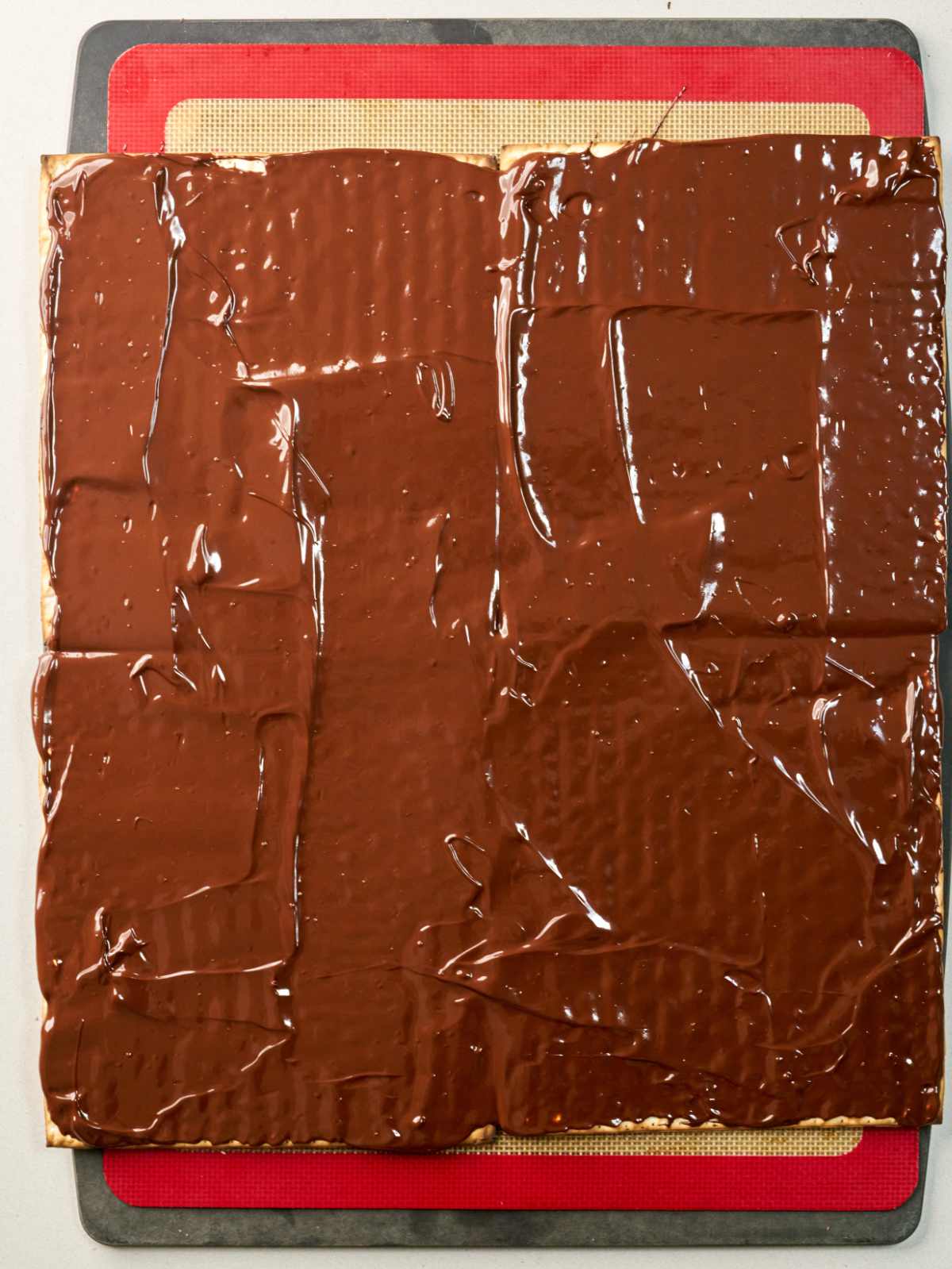 A large square matzo covered in melted chocolate on top of a baking mat.