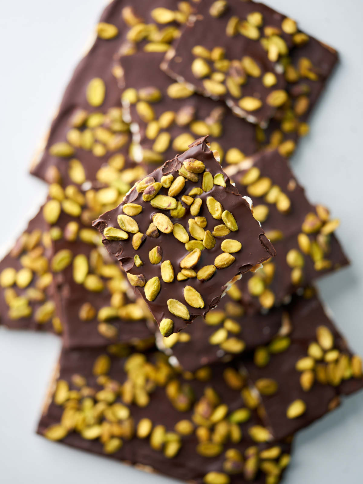 A pile of square pieces of matzo with chocolate and pistachios.