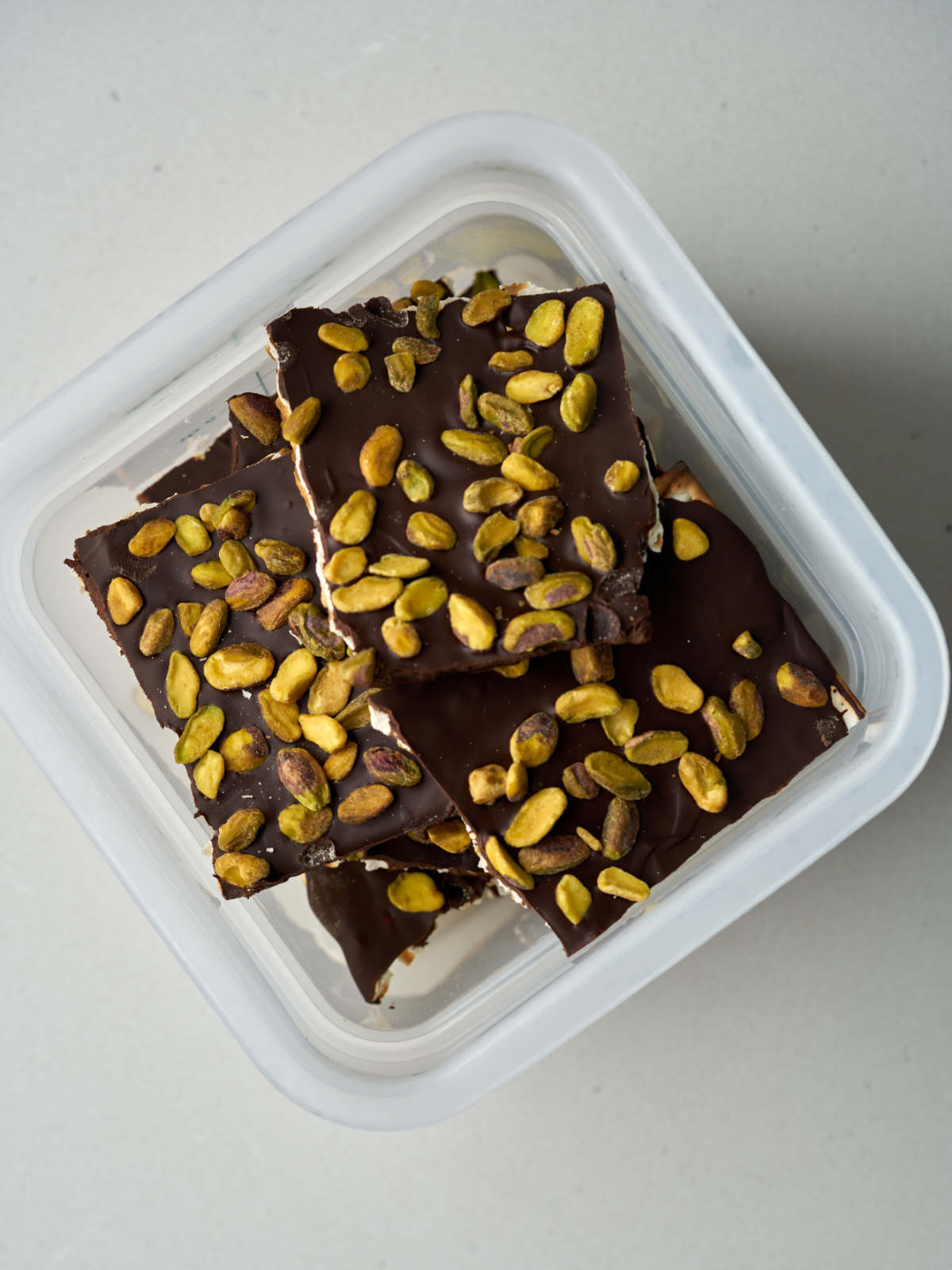 Overhead view of square pieces of matzo and chocolate in a plastic storage container.