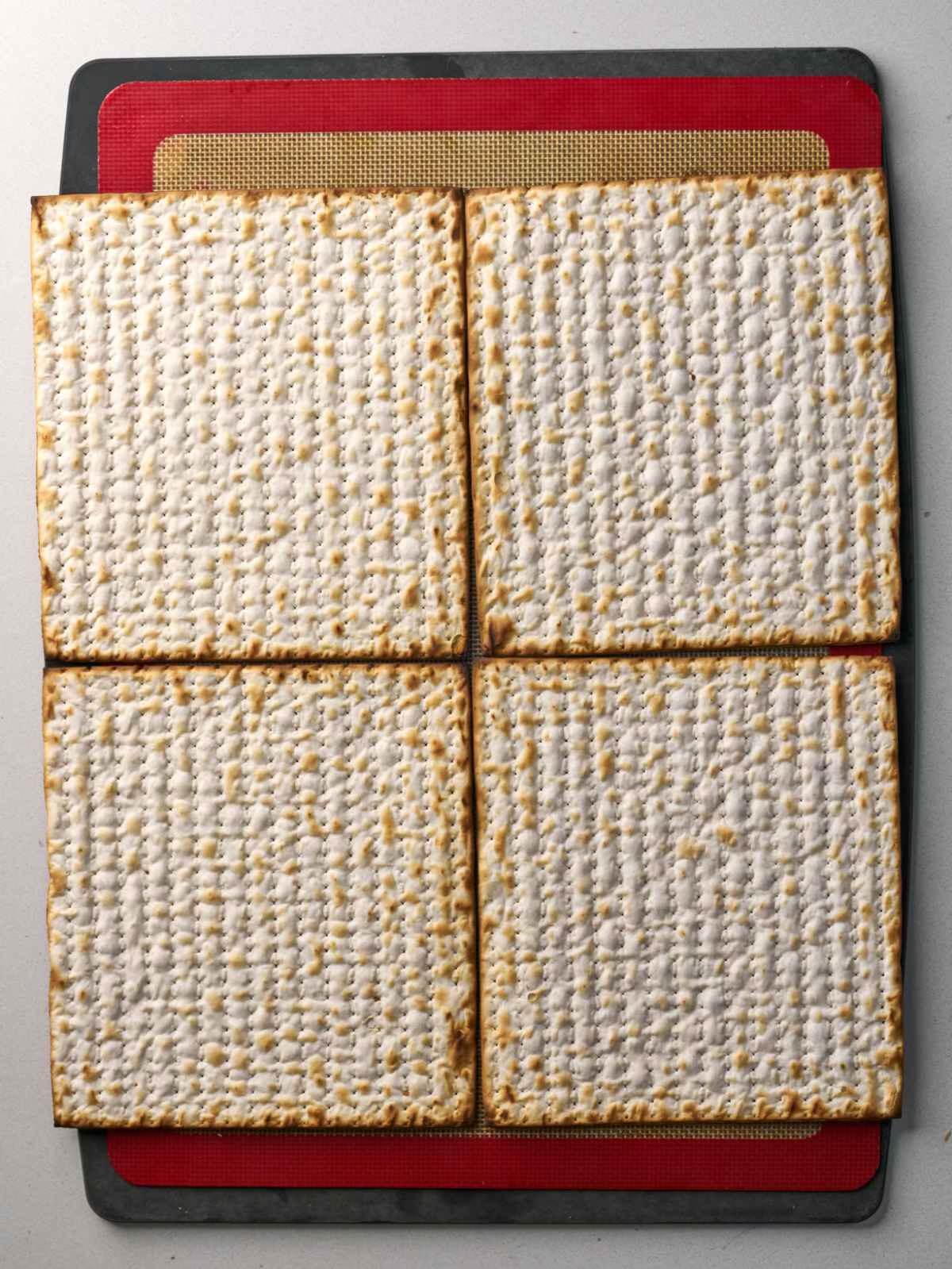 Four pieces of matzo laid on a baking sheet in one big square.