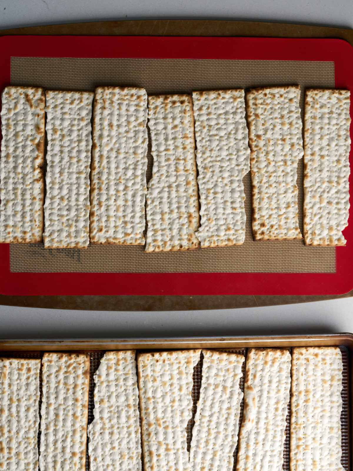 Plain pieces of matzo bread on a silpat baking mat on a sheet pan.