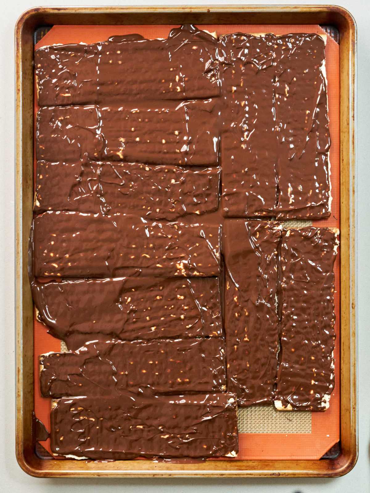 Pieces of matzo bread covered in melted chocolate on top of a sheet pan.