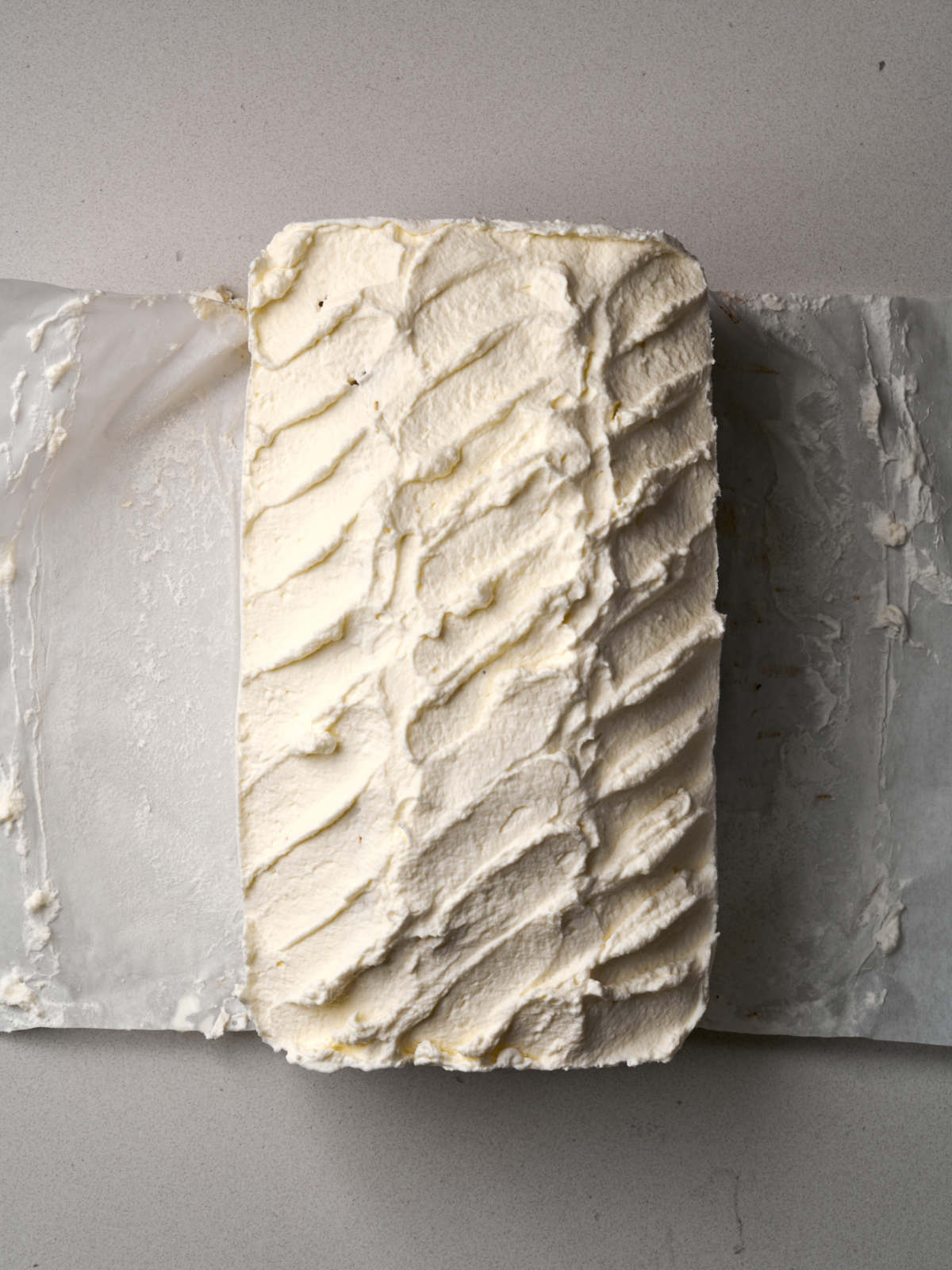 Top view of a loaf-shaped cake on parchment paper with a whipped cream design.