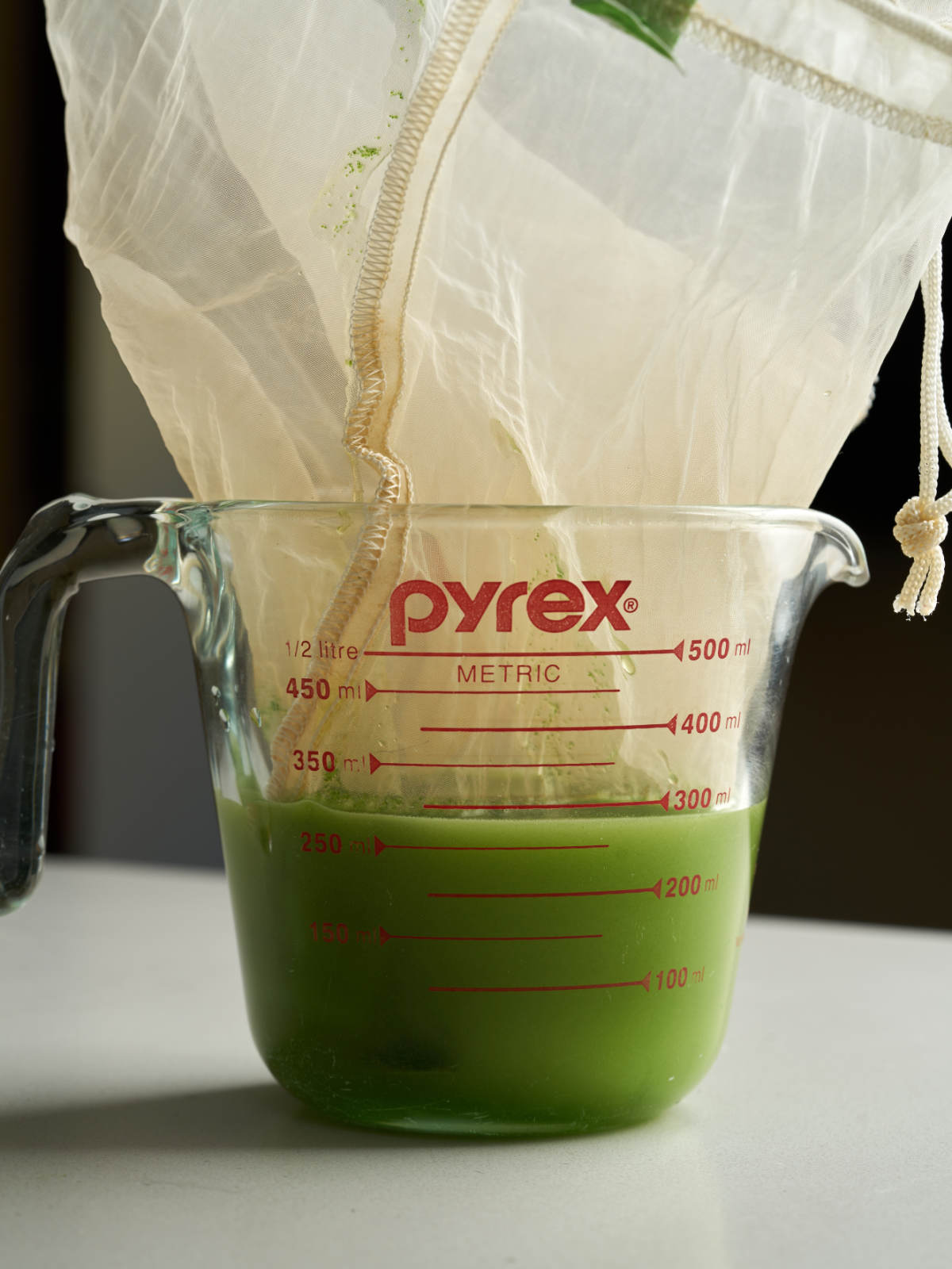 Green liquid in a liquid measuring cup with a nut milk bag inside of it.