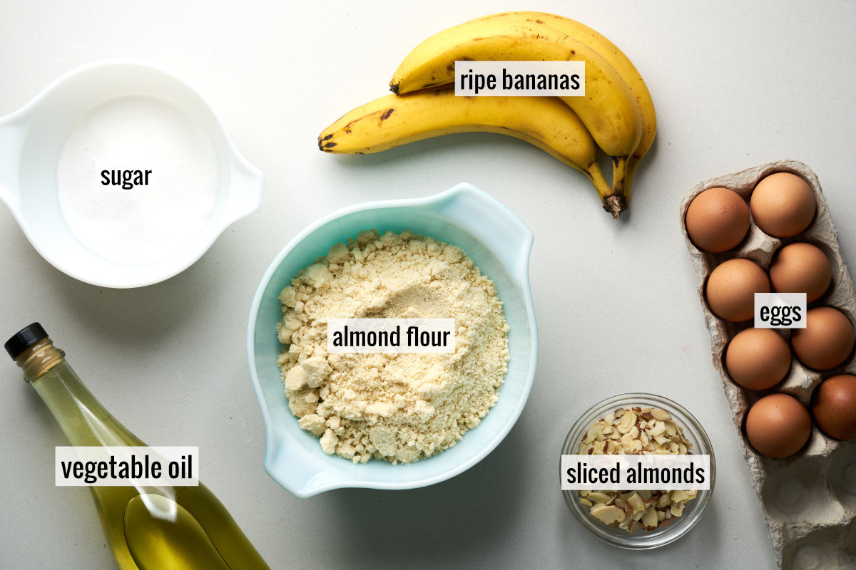 Top down photo of ingredients including sugar, bananas, eggs, almond flour, class almonds, and a vegetable oil