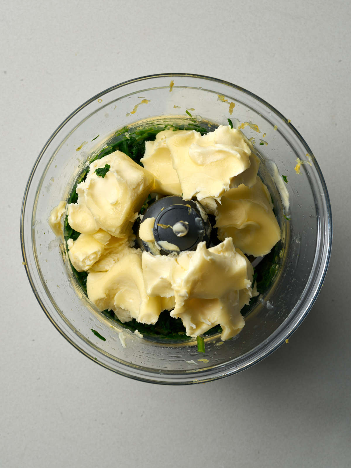 Large chunks of yellow butter on top of greens in a food processor