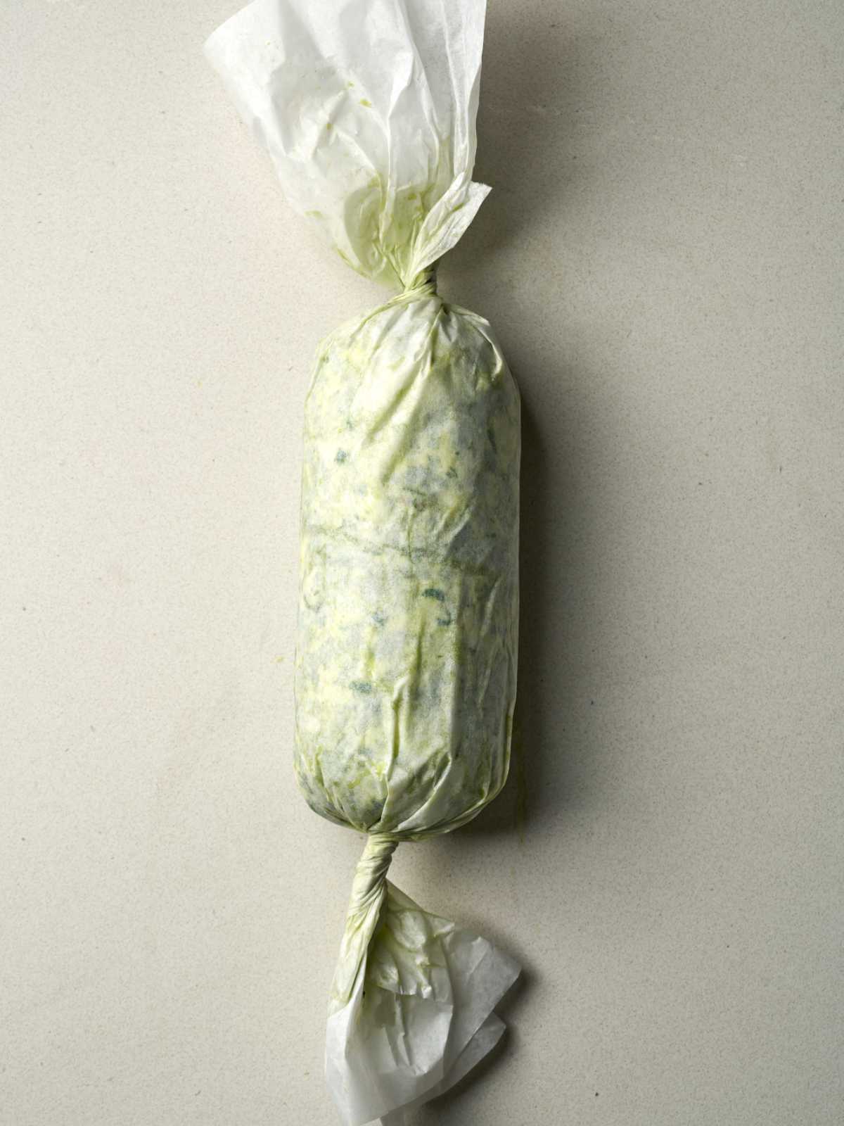 A log of green and beige butter wrapped tightly in parchment paper