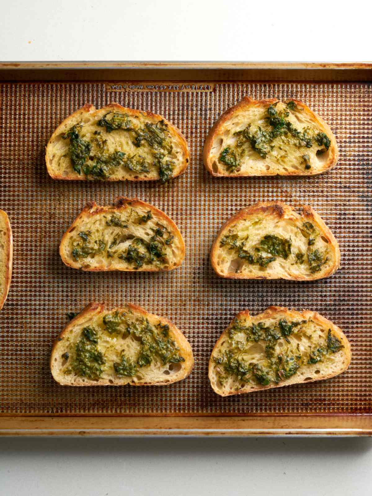 Small pieces of toast on a metal pan with melted butter on top