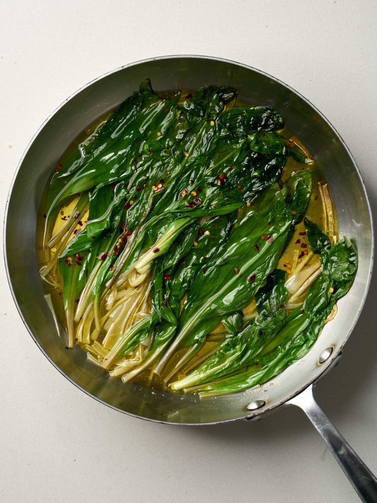 Green ramps wilted in oil in a large silver saucepan