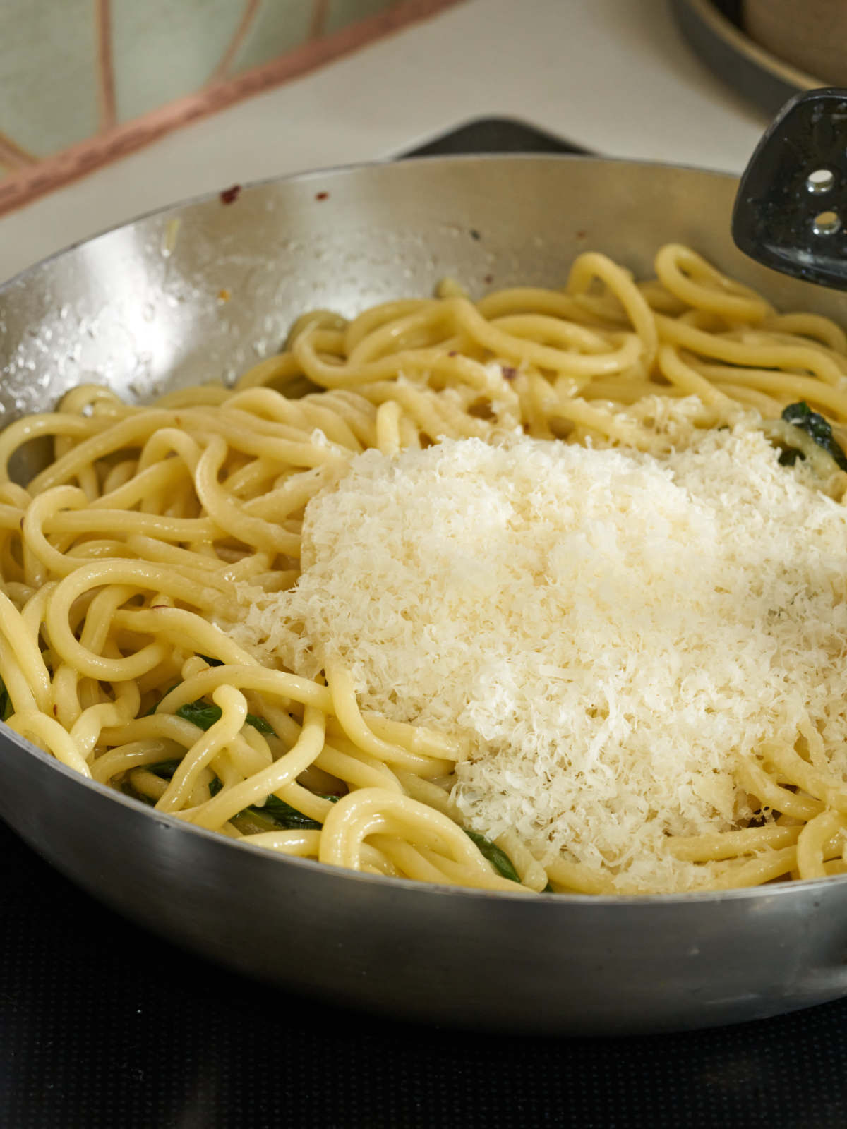 Pasta noodles in a silver saucepan with a large mound of Parmesan cheese in the middle