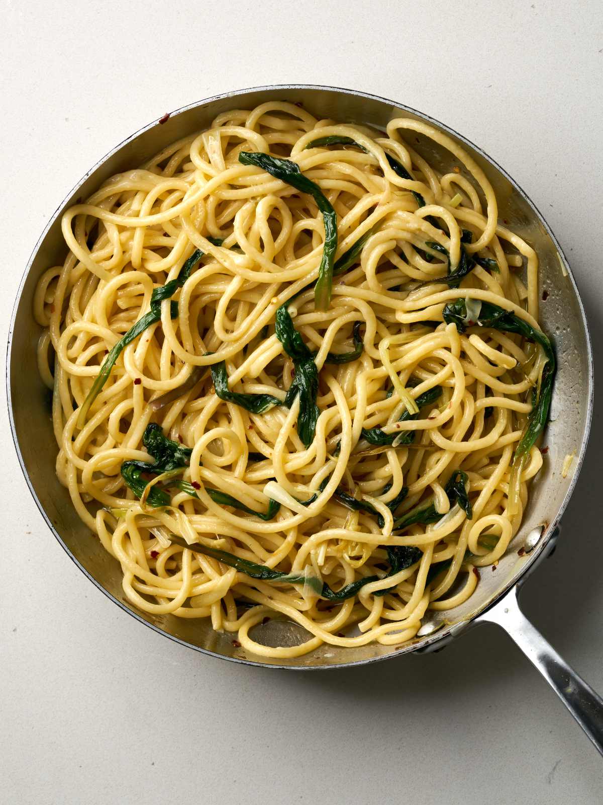 Cooked bucatini pasta with greens in a large silver sauce pan