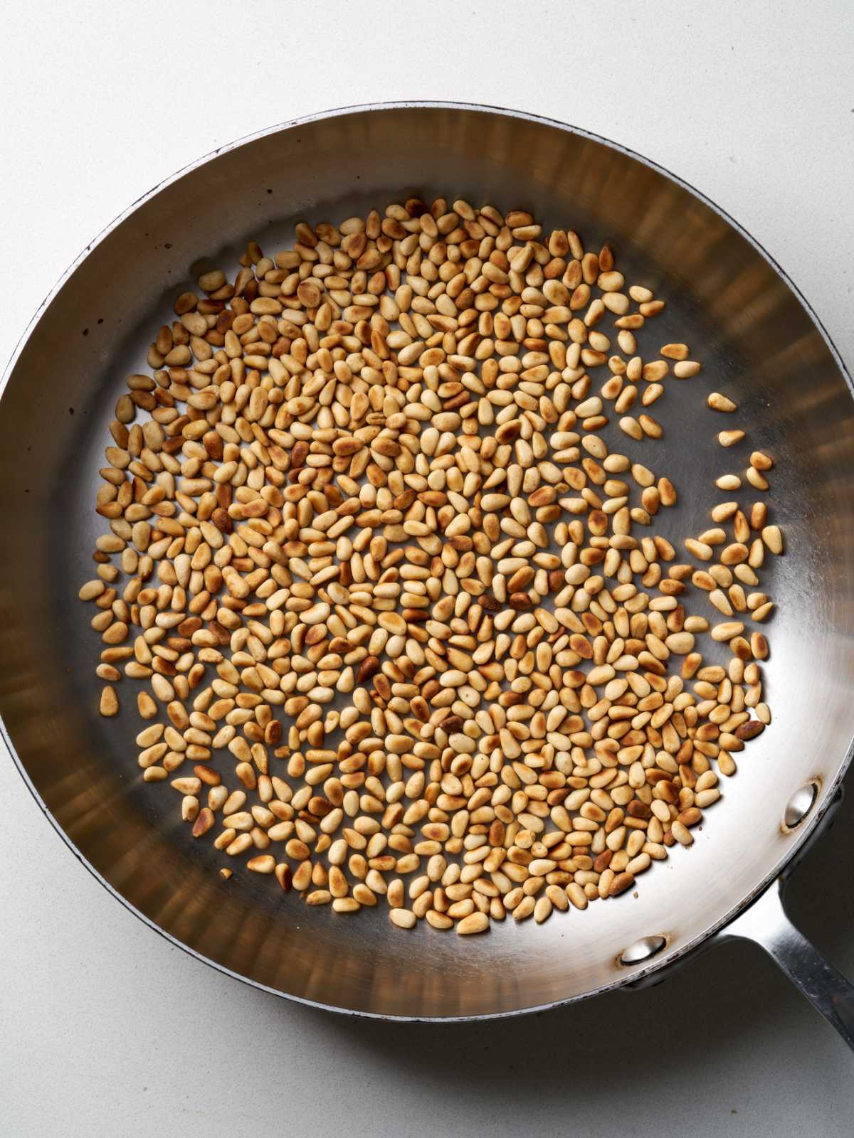 Pine nuts toasting in a large silver pan.