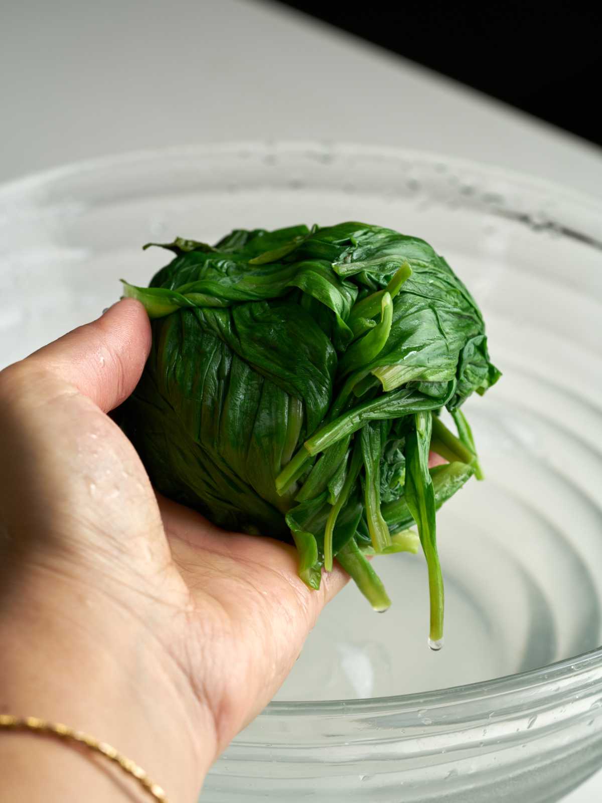 Hand holding a compact ball of wet green leaves.