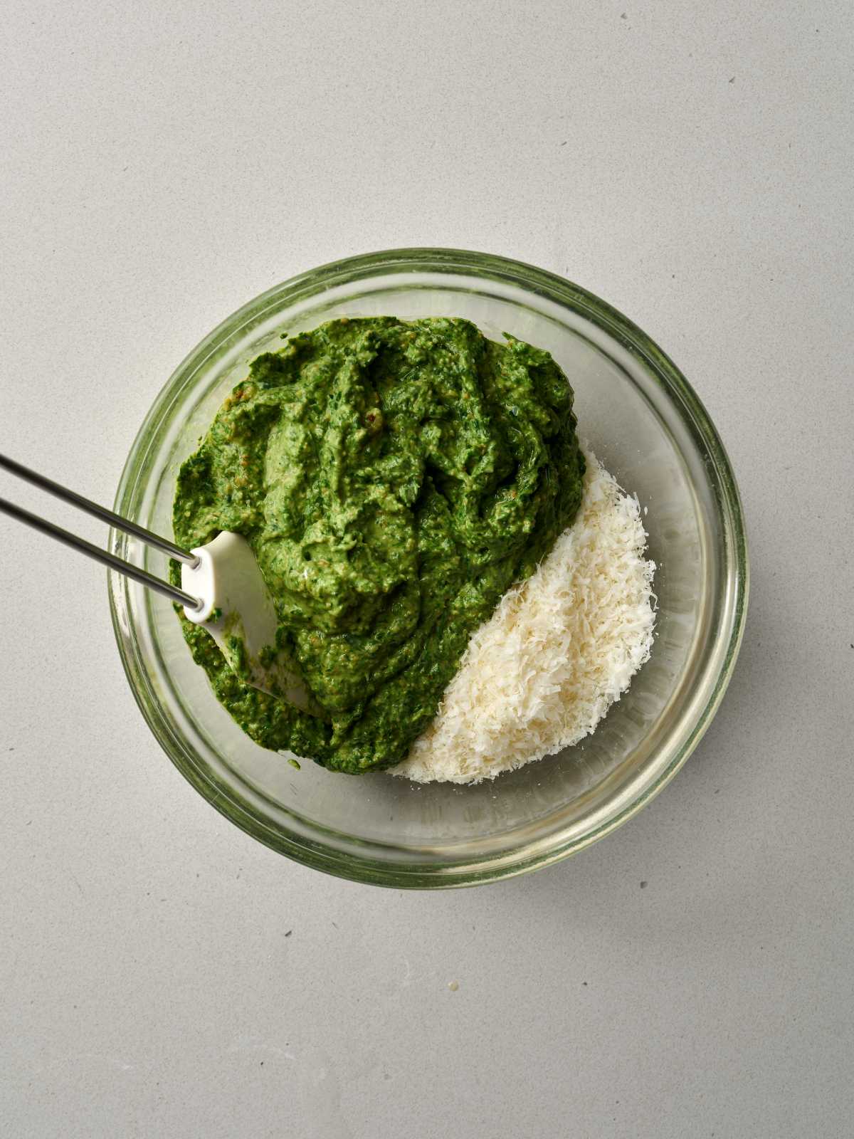 Glass bowl containing green pesto and a mound of shaved Parmesan.