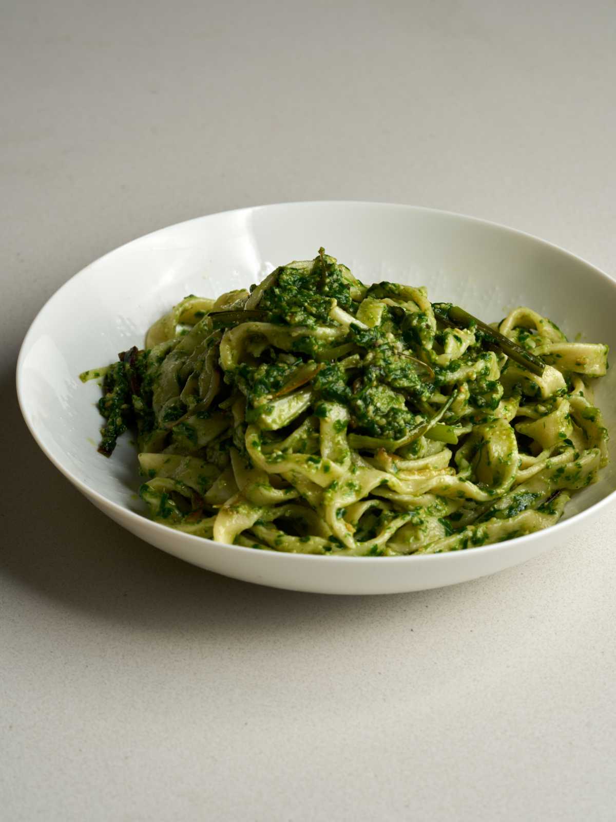 Side view of a mound of pasta with green pesto sauce on a white plate.