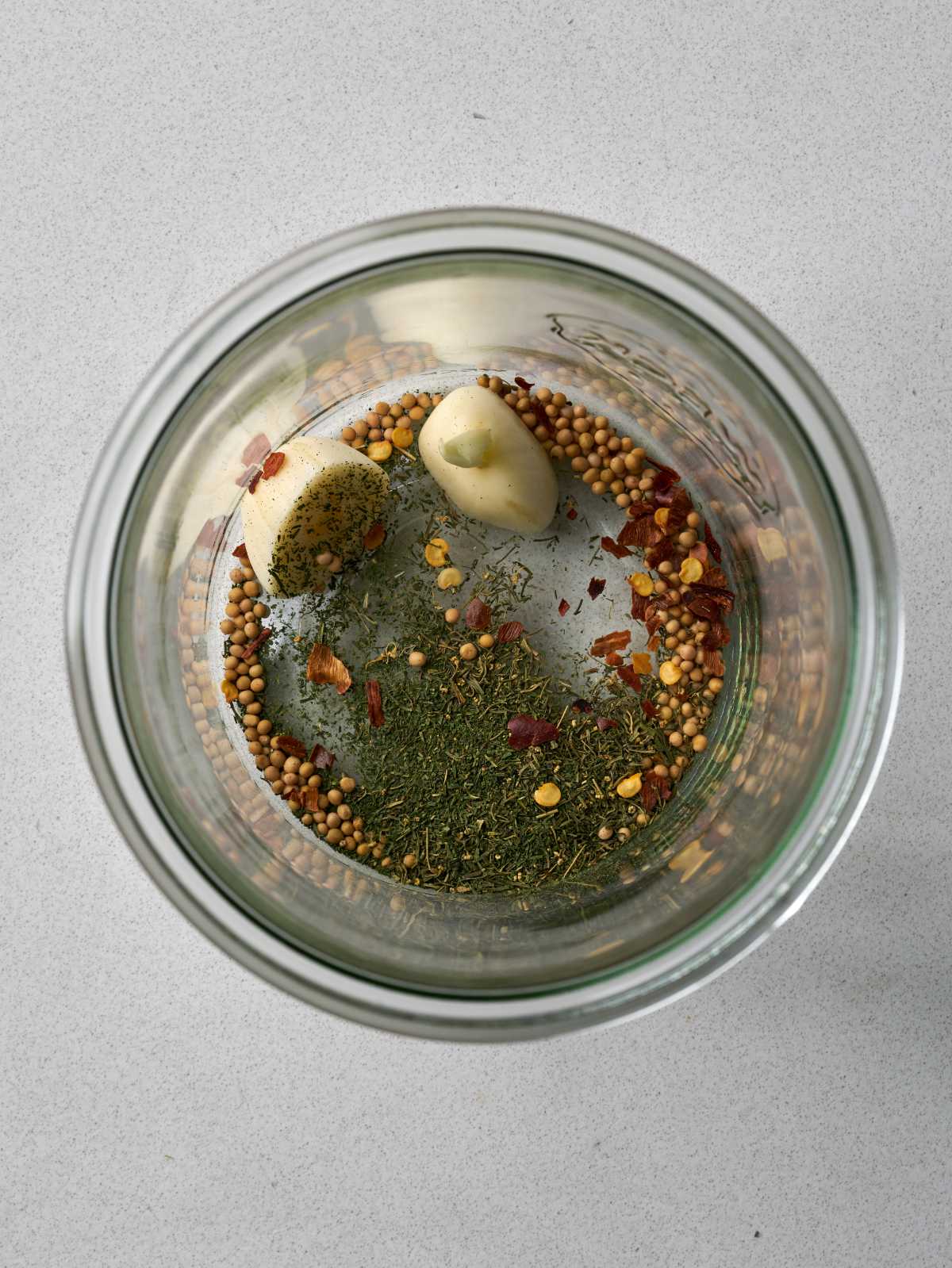 Glass jar containing garlic, mustard seeds, red pepper flakes, and dried dill