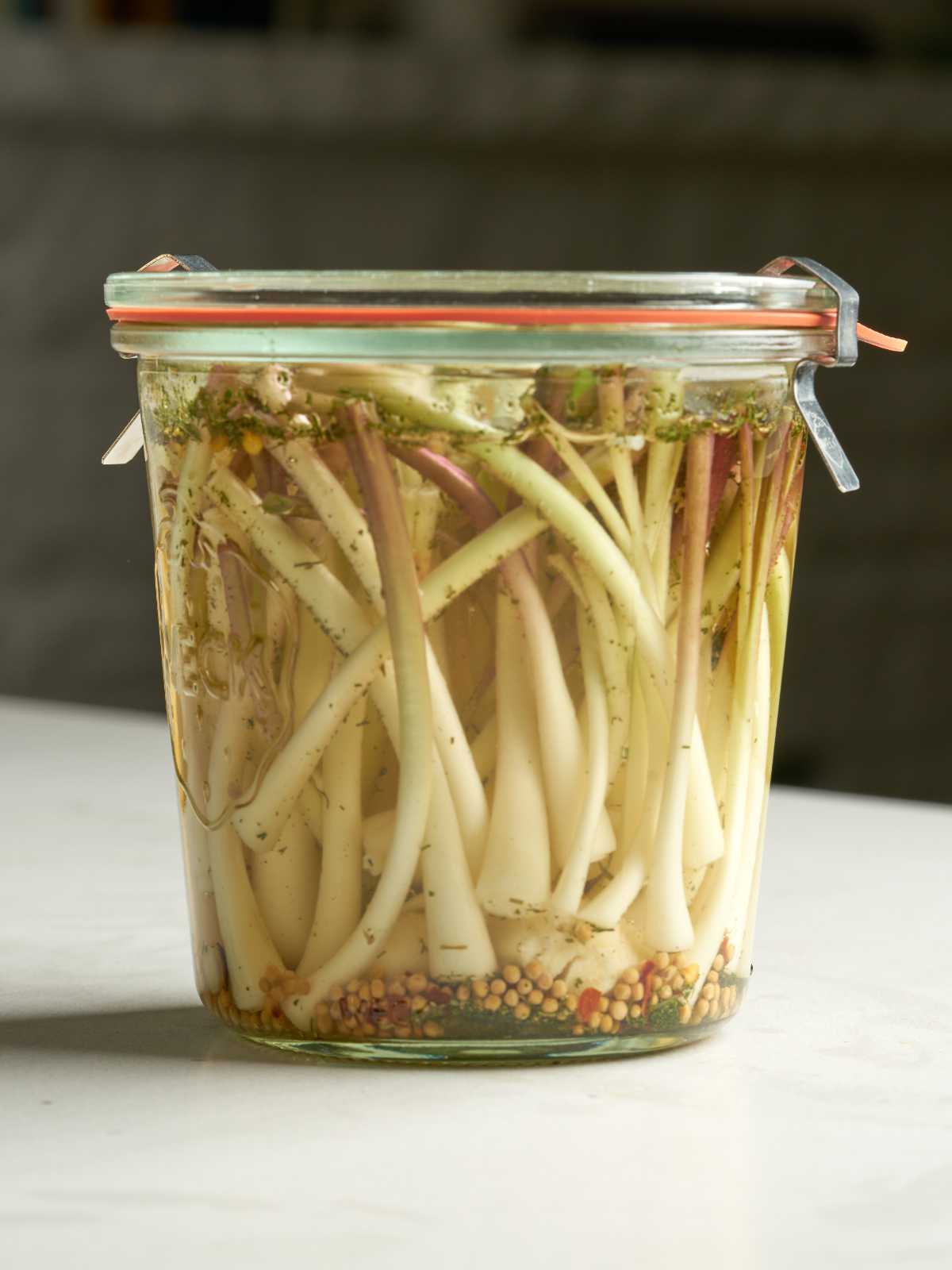 White ramp bulbs in a clear liquid with herbs and spices in a sealed glass jar