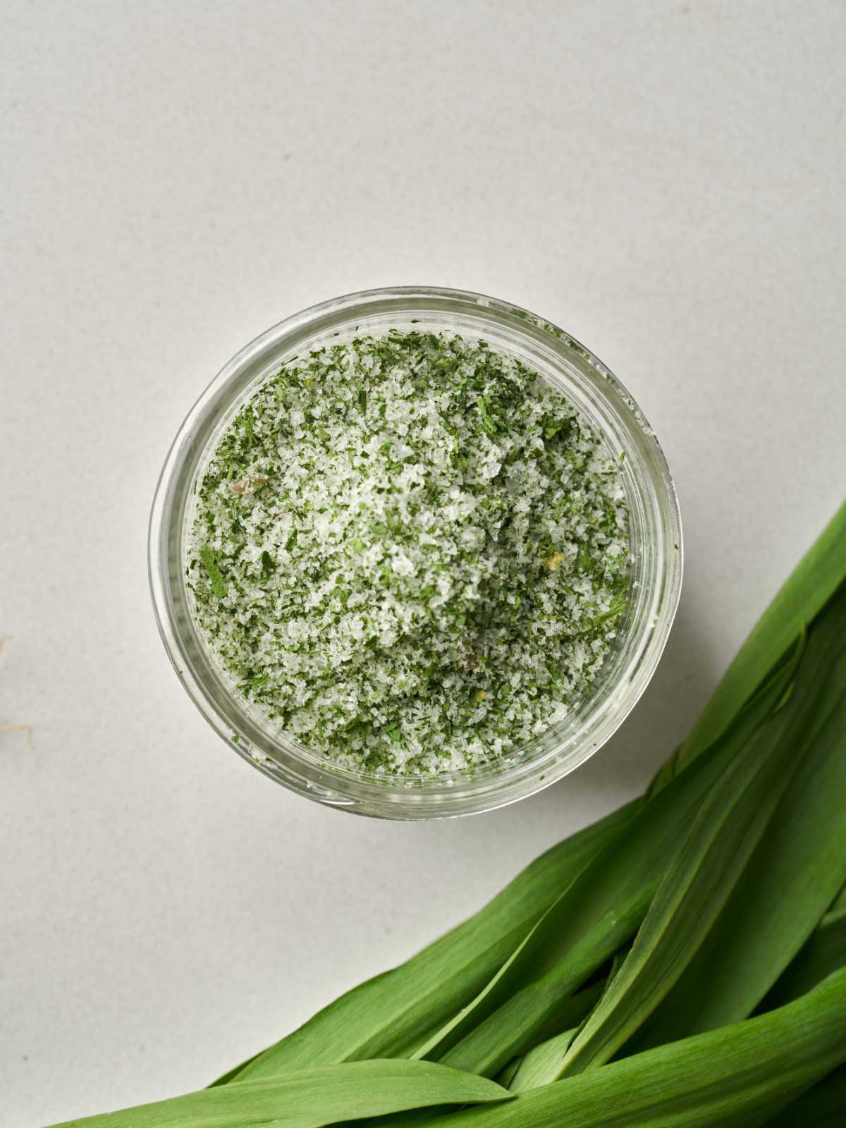 Are overhead view of green and white salt and a small glass jar with green leaves below