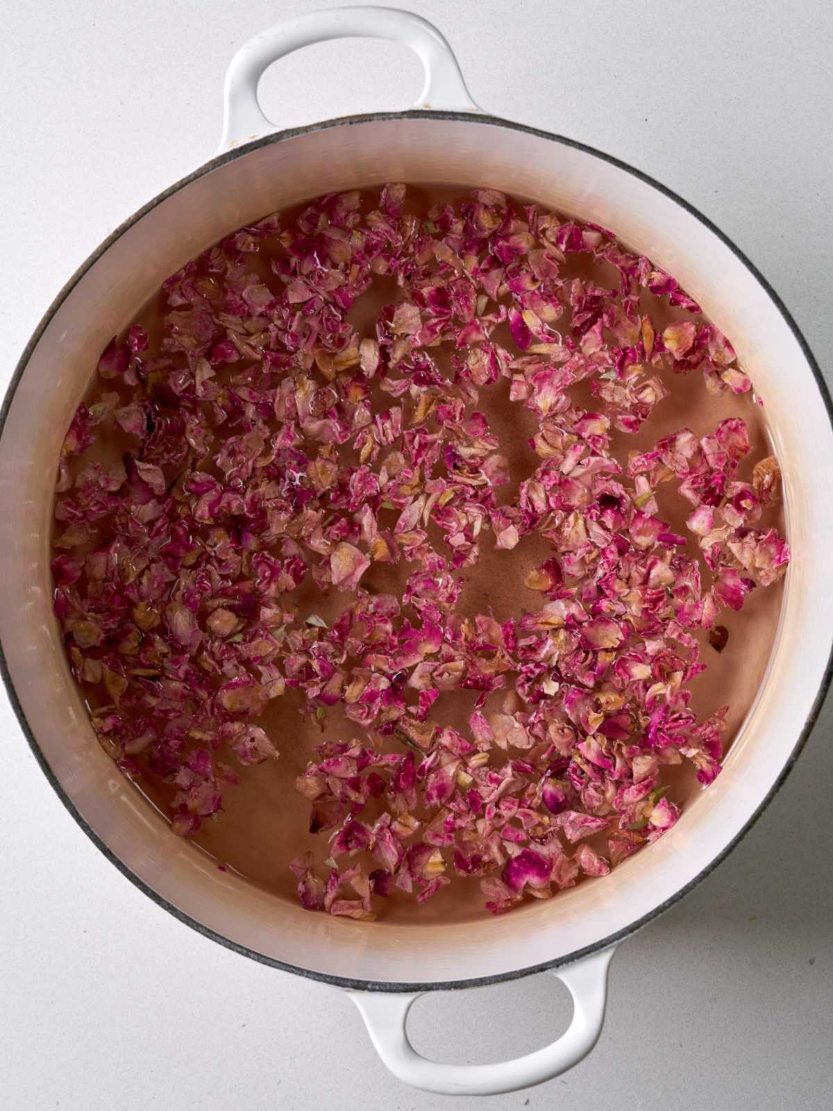 White pot filled with water and tiny pink rose petals.