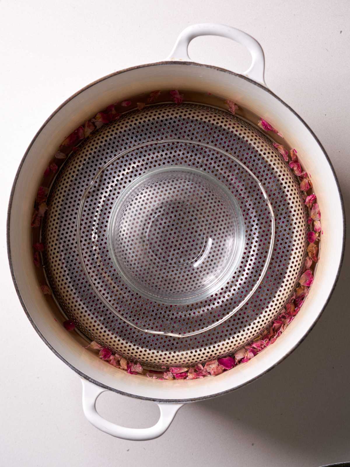 White pot filled with an inverted metal strainer and topped with a small glass bowl with tiny rose petals surrounding the metal strainer.