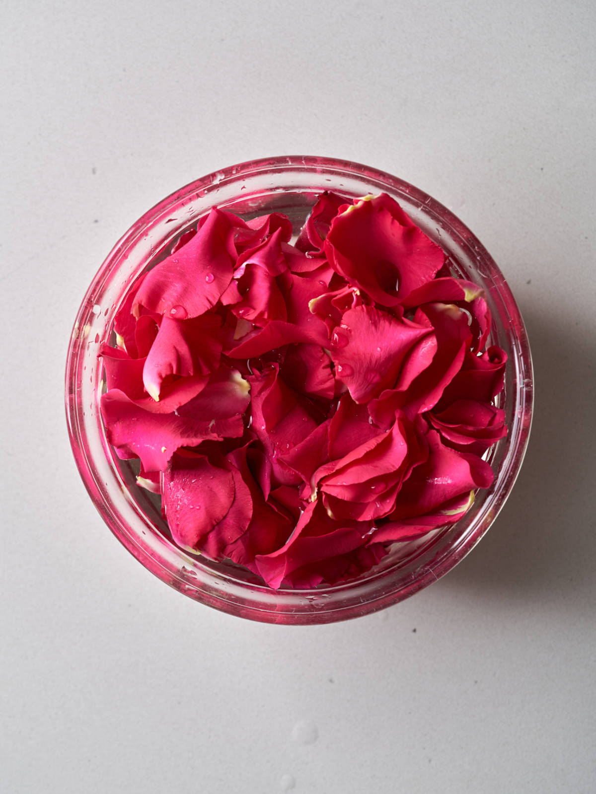 Glass bowl filled with water and hot pink rose petals.