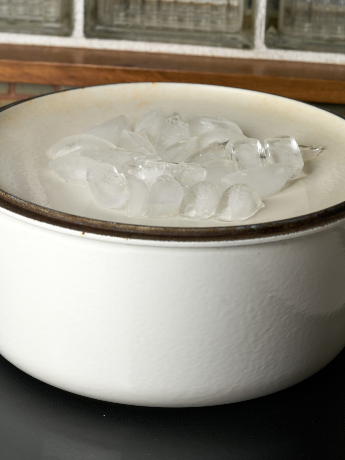 White pot on a black cooktop with an inverted lid filled with ice.