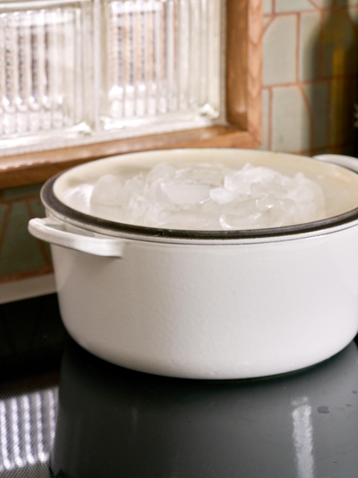 White pot on a black cooktop with an inverted lid filled with ice.