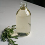 Large glass bottle of clear simple syrup with rosemary beside it.