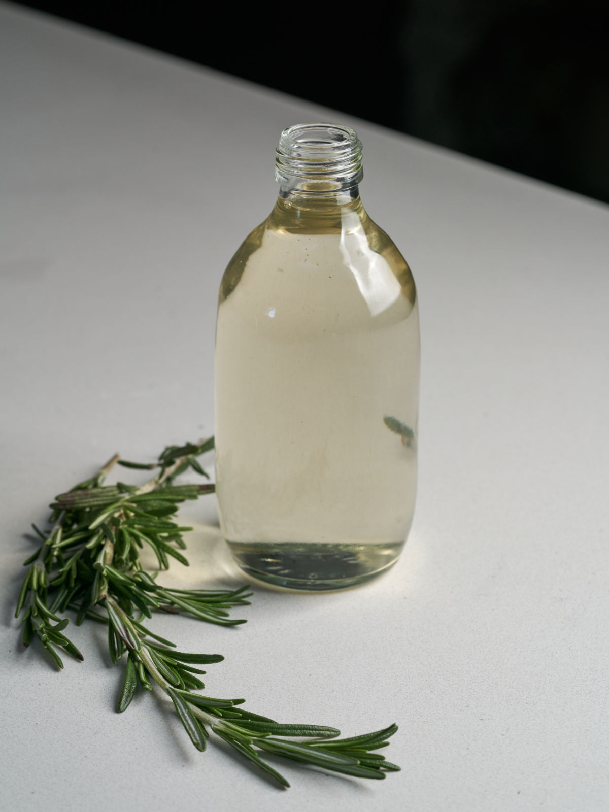 Large glass bottle of clear simple syrup with rosemary beside it.