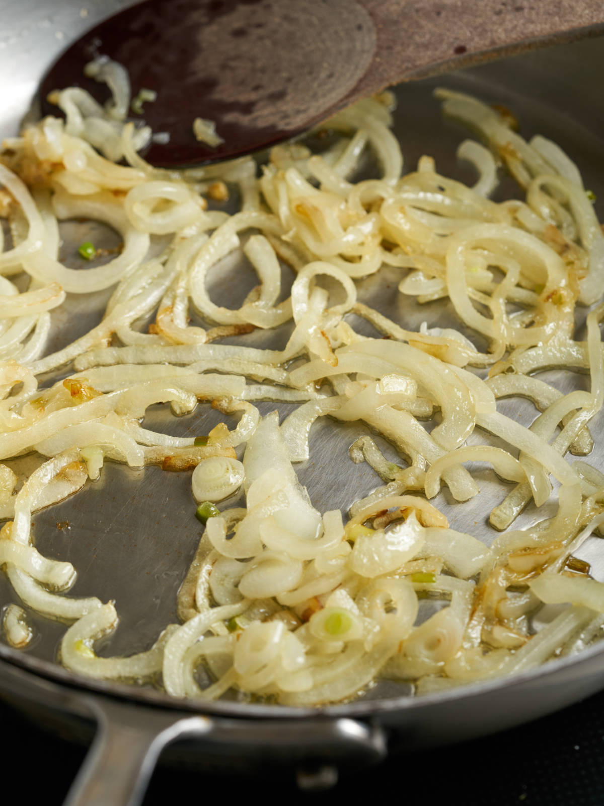 Fried onions in a large silver pan with a wooden spoon.