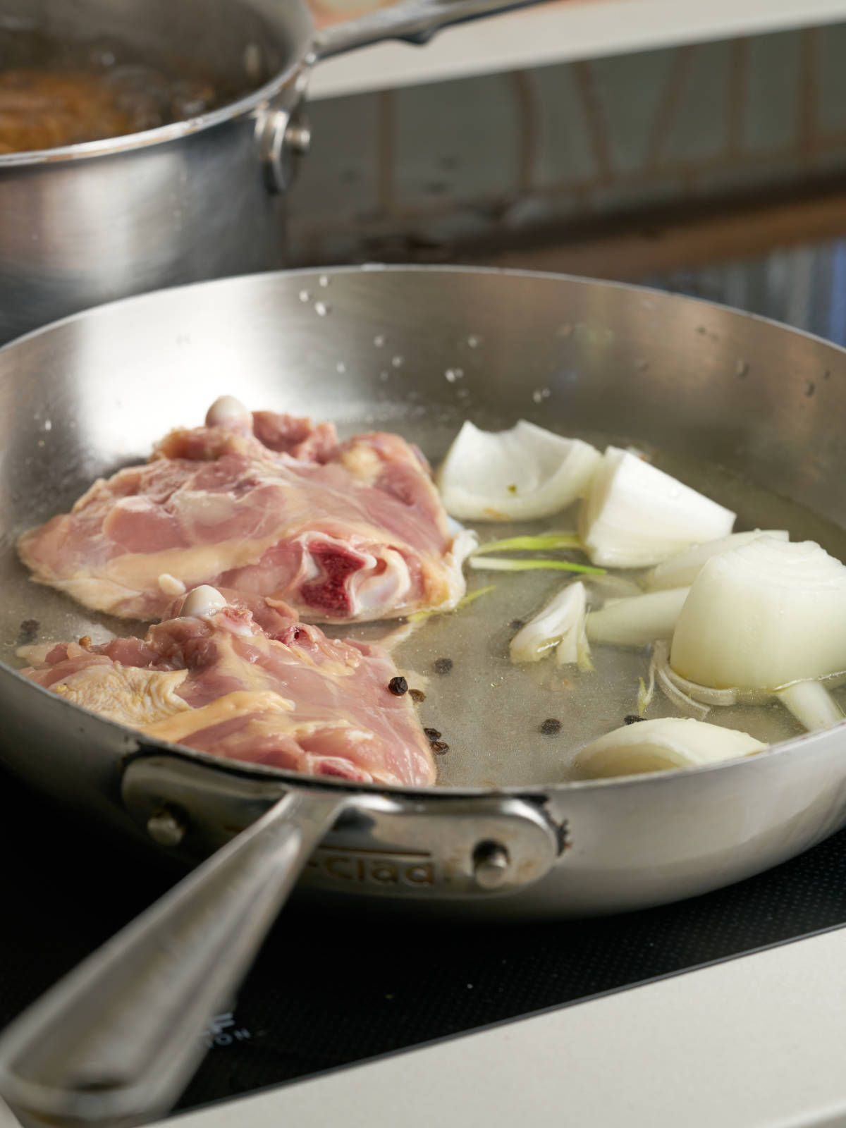 Raw chicken thighs with quartered onions in a large silver frying pan.