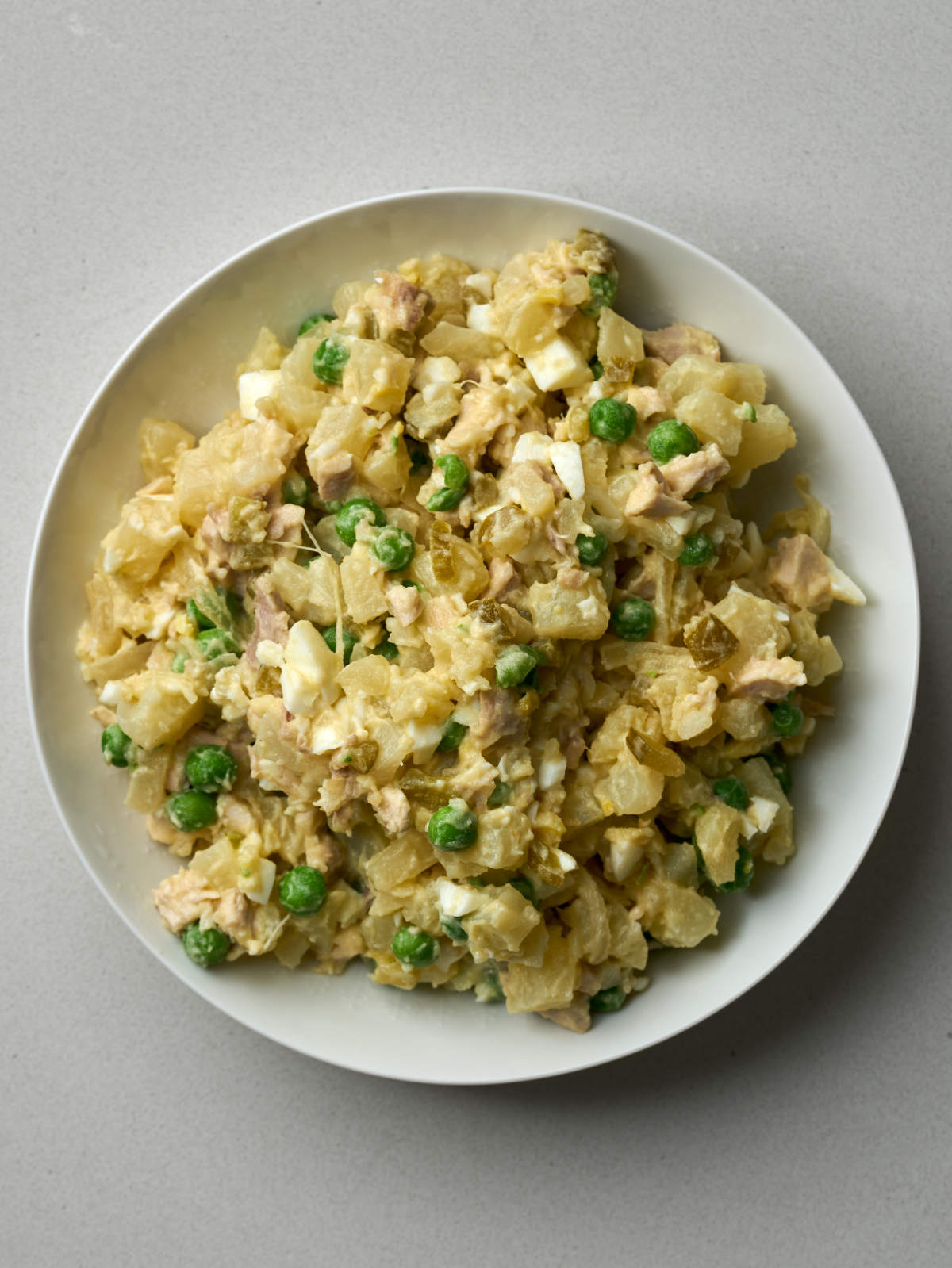 A mix of diced chicken, potatoes, peas, eggs and pickles on a white plate.