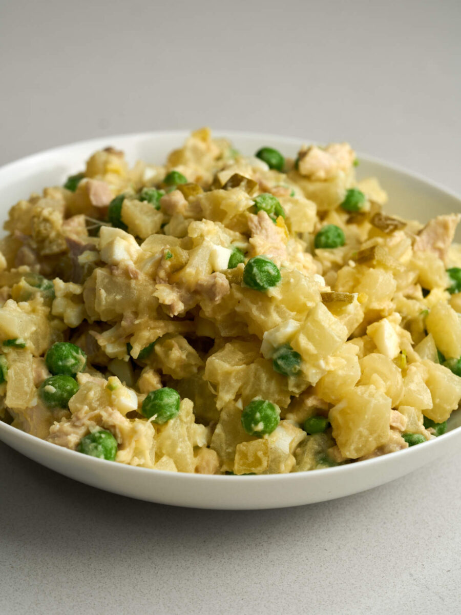 Side view of a mix of diced chicken, potatoes, peas, eggs and pickles on a white plate.