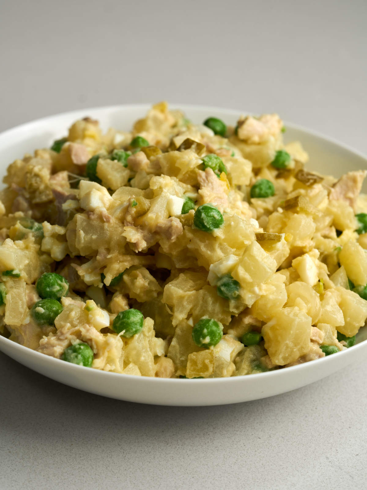 Side view of a mix of diced chicken, potatoes, peas, eggs and pickles on a white plate.