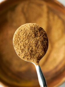 Spice filled silver spoon over a wooden bowl.
